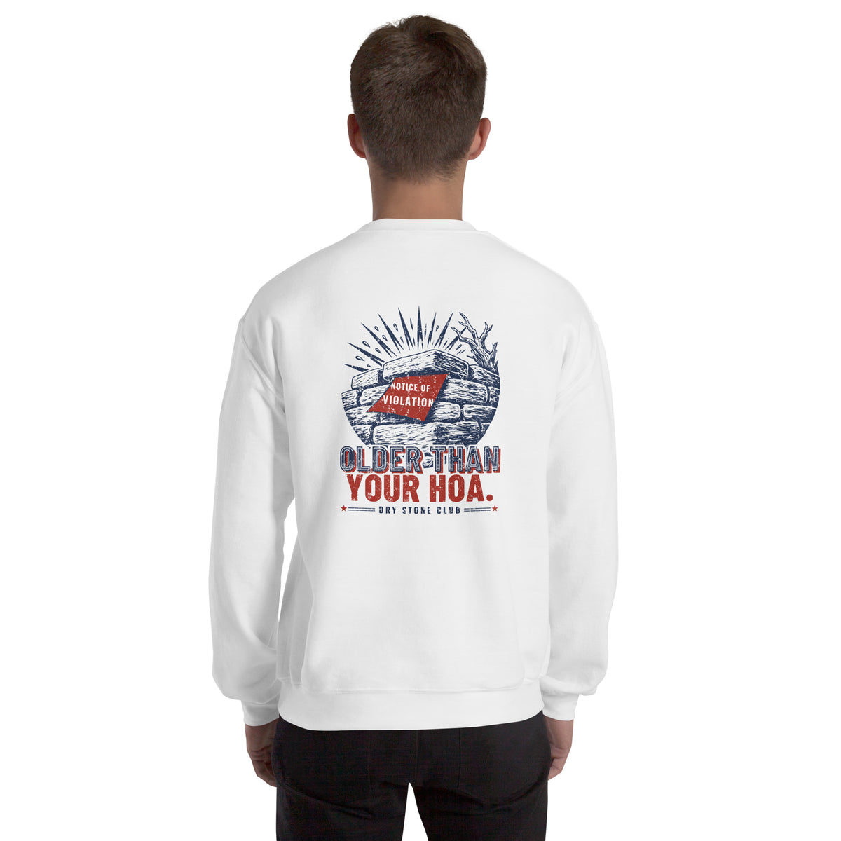 Man seen from behind in the white Older Than Your HOA sweatshirt, navy and red stone wall print across the upper back.