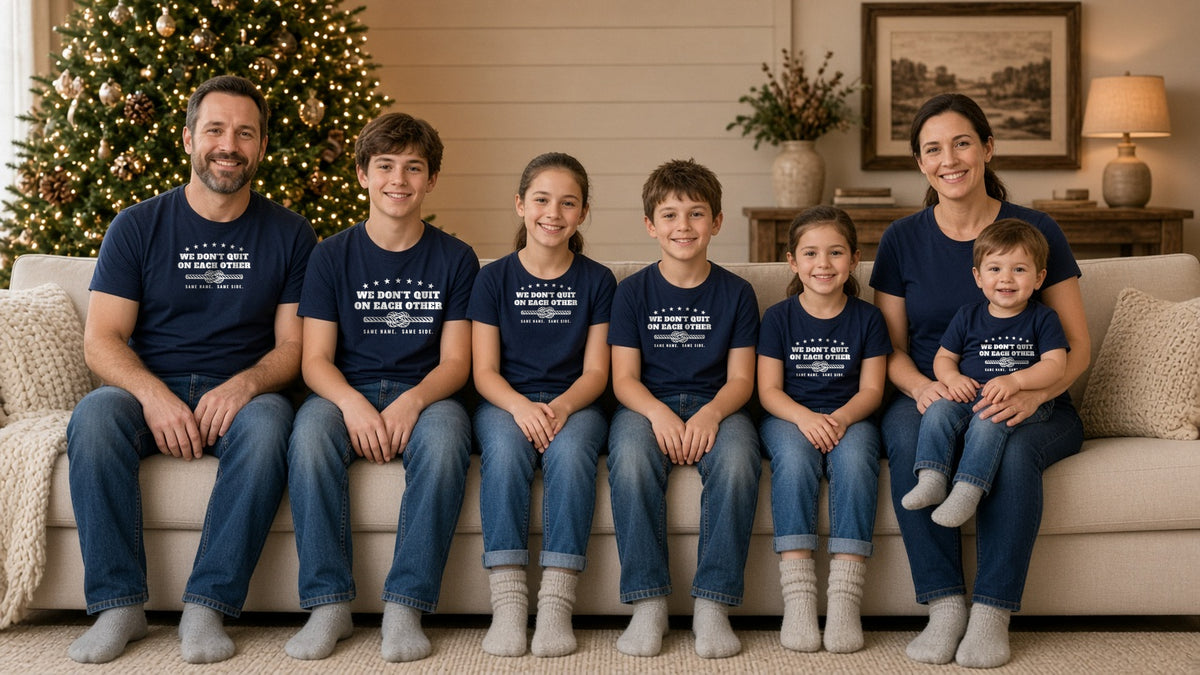 Family of eight in matching navy We Don't Quit on Each Other tees sitting on a couch beside a lit Christmas tree